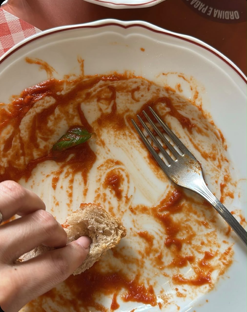 Assiette presque vide saucée avec un morceau de pain, une fourchette et une feuille de basilic dans la sauce tomate