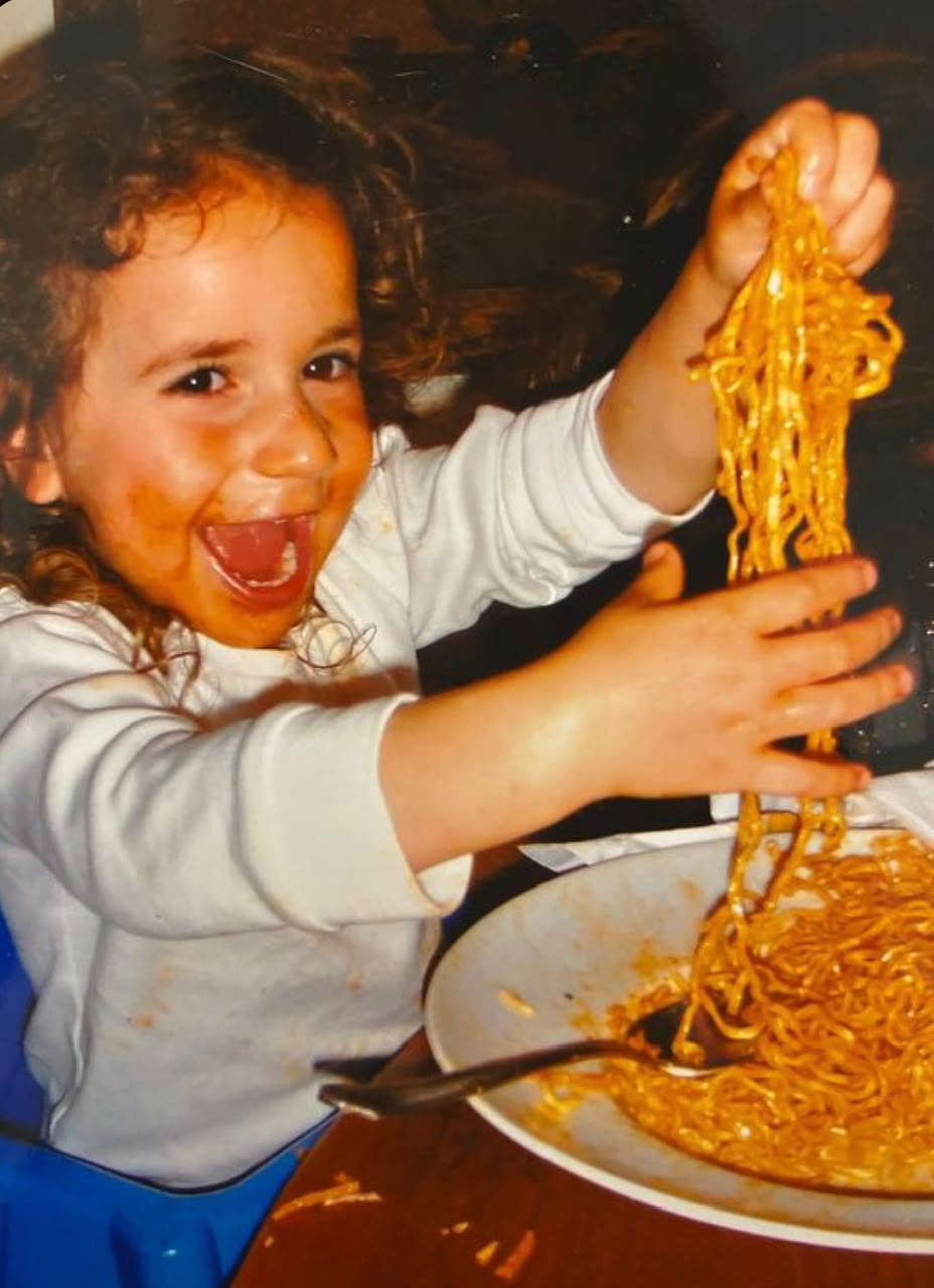 Enfant éclatant de rire en soulevant une poignée de spaghetti au-dessus de son assiette