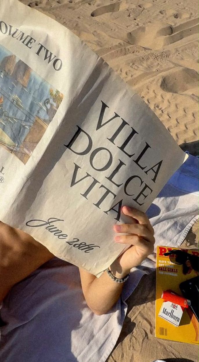 Sur une serviette de plage, une personne lit un journal titré Villa Dolce Vita
